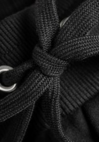 Black woven fabric with a twisted lace tied in a knot, featuring a metal grommet. The texture is smooth and dense, showcasing fine stitching.