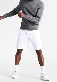 Grå sweatshirt med rund hals och ribbade muddar och nederkant, kombinerad med vita shorts. Vita sportskor med grå detaljer och vita strumpor.