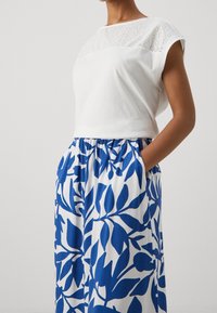 Valkoinen puuvillapaita, jossa on reikäkuviointi kaula-aukossa, yhdistettynä sinivalkoiseen kukkakuosiseksi hameeksi, jossa on joustava vyötärö ja taskut.