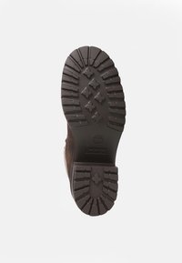 Suela de bota de goma marrón con surcos profundos y un diseño estampado. Presenta el logo de Timberland de manera destacada en el centro.