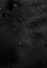 Gros plan sur un tissu noir texturé avec des gouttes d'eau perlant à la surface, mettant en avant sa propriété hydrofuge.