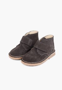 Stivali in suede grigio scuro con una fascia in velcro, punte tonde e suole marrone chiaro. Presentano dettagli cuciti lungo la suola.