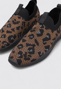 Zapatillas elásticas sin cordones con un diseño de estampado leopardo marrón y negro, con una parte superior de punto texturizado y una suela de goma negra flexible.