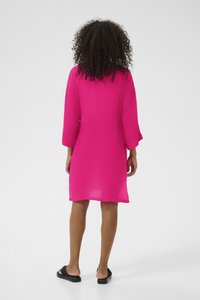 Vestido suelto rosa con mangas de tres cuartos, tejido texturizado, hasta la rodilla y con la cintura ceñida. Combinado con sandalias negras.