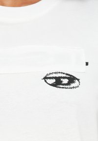 Άσπρο βαμβακερό μπλουζάκι με μαύρο γραφικό σχέδιο που μοιάζει με μάτι και μια οριζόντια λευκή λωρίδα στο ύψος του στήθους με ραφές.