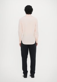 Lys rosa langærmet skjorte med lige kant, knapmanchetter og rygåge, parret med sorte bukser og sko. Simpelt design og pasform.