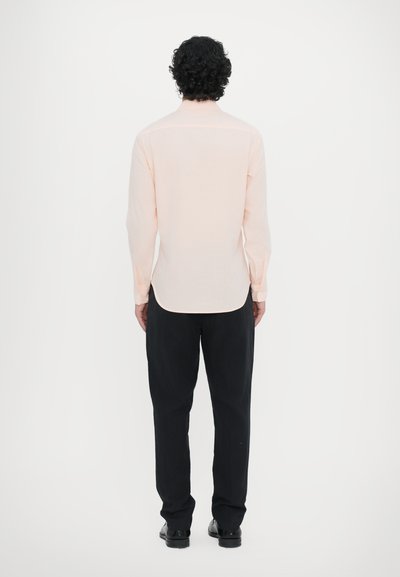 Lichtroze langetermijn overhemd met een rechte onderrand, knoopmanchetten en een achterpaneel, gecombineerd met zwarte broek en schoenen. Eenvoudig ontwerp en pasvorm.