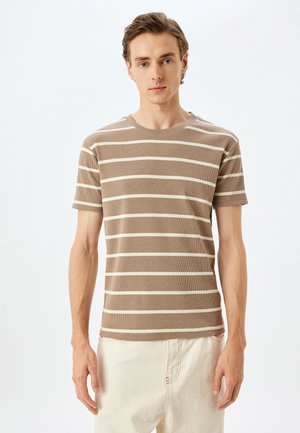 Brun og creme stribet kortærmet t-shirt, rund hals, ribbet tekstur, tætsiddende design, båret med lyse bukser.