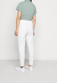 Světle zelený top s krátkým rukávem a detaily ve tvaru klíčové dírky na zadní straně, spárovaný s bílými kalhotami s elastickým pasem a bílými teniskami s mátovými akcenty.