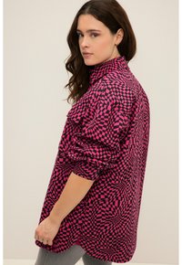 Camisa de manga larga en rosa y negro con un patrón a cuadros. Presenta un cuello alto y un corte relajado con mangas enrolladas. Textura de tela suave.