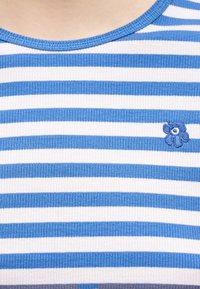 Κοντινή λήψη υφάσματος με οριζόντιες ρίγες σε μπλε και λευκό χρώμα, με ένα μικρό κεντημένο μπλε λουλούδι κοντά στη λαιμόκοψη ενός πουκαμίσου.