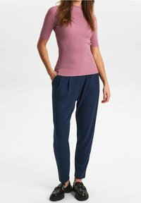 Rosa ribbad kortärmad topp i kombination med marinblå veckade byxor. Svarta slip-on-skor med detaljer i guld.