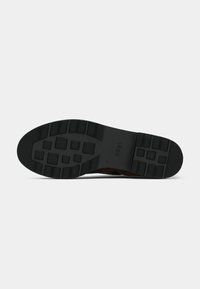 Semelle en caoutchouc noir avec un motif de bande de roulement texturé et un logo, présentant un dessus en suède marron avec des accents cousus.