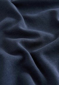 Marineblaue Baumwollstoff mit einer glatten Textur, der weiche Falten und subtilen Stretch aufweist und seine Leichtigkeit und Flexibilität unterstreicht.