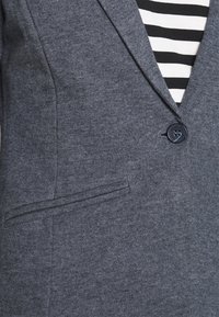 Grå blazer i texturerat tyg med slim fit, med en enda blå knapp, notch-krage och en sidficka. Randig skjorta synlig under.