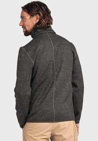 Strukturierte schwarz-weiße Jacke mit hohem Kragen, die eine glatte Oberfläche und sichtbare Nähte aufweist, getragen über beigen Hosen.