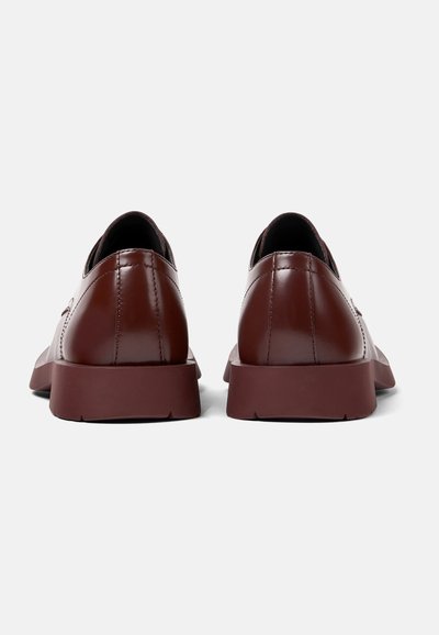 Scarpe in pelle marrone con finitura lucida, texture liscia, punta arrotondata e una suola spessa e solida di colore bordeaux. Design minimalista, senza decorazioni.
