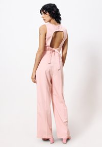 Roze mouwloze jumpsuit met brede pijpen, open rugontwerp en stoffen strik detail in de taille. Gladde textuur en op maat gemaakte pasvorm.