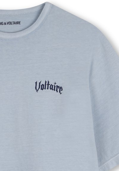 T-shirt en coton bleu clair avec un col rond, arborant un logo texte "Voltaire" brodé en bleu foncé sur la poitrine gauche.