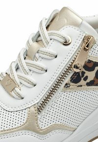 Baskets blanches avec accents dorés, panneaux perforés texturés, fermeture éclair décorative et détail imprimé léopard sur le côté.