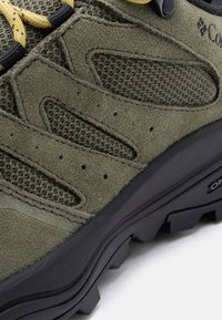 Κοντινό πλάνο πεζοπορικού μποτάκι σε ελιά πράσινο χρώμα με πάνελ από σουέτ, ένθετα από δίχτυ, κορδόνια κίτρινου και μαύρου χρώματος και ανθεκτική μαύρη σόλα.