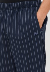 Marineblauwe broek met verticale witte strepen, elastische tailleband, zijzakken en een geborduurd 'MOP' logo op de linkerheup.