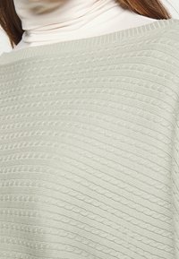 Ljusgrön strukturerad tröja med ribbat ok och ett vågigt mönster genom hela tyget, som visar en mjuk stickad kvalité.
