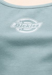 Ανοιχτό γαλάζιο ριγωτό ύφασμα με ξεθωριασμένο λευκό κυκλικό λογότυπο και μερικώς αναγνώσιμο κείμενο στη μέση.