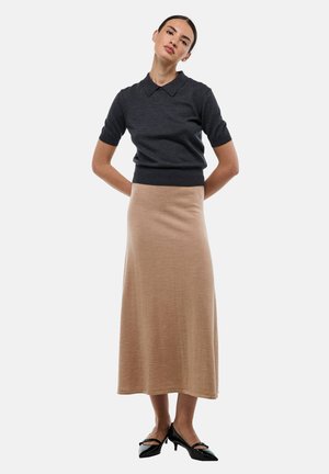 Polo en tricot à manches courtes gris foncé avec un col, associé à une longue jupe marron clair. Des chaussures à talons hauts noires complètent la tenue.