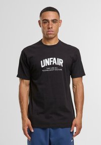 Zwarte katoenen t-shirt met gedurfde witte tekst "UNFAIR" en kleinere tekst eronder. Korte mouwen en een klassiek ronde hals ontwerp.