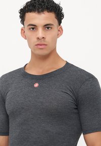 Graues T-Shirt mit kurzen Ärmeln, rundem Ausschnitt, geripptem Material und einem kleinen roten Logo auf der linken Brust. Gerade geschnittenes Design.