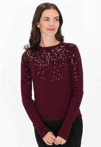 Pull bordeaux avec une texture côtelée et des détails en sequins sur la partie supérieure. Les manches longues possèdent des poignets ajustés.