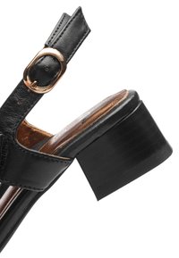 Sort læder sandal med åbne tæer, guldspænde og en chunky blokhæl, der viser siden og sålens detaljer.