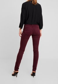 Burgundy skinny jeans with a mid-rise fit, paired with a loose black blouse. The jeans have two back pockets and a smooth texture.