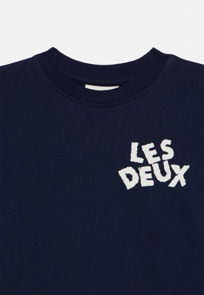 Тъмносиня тениска с бял текст "LES DEUX" в удебелен, неправилен шрифт на лявата част на гърдите.
