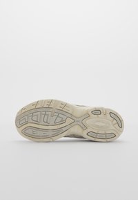 Sula av en beiga och ljusgrå sneakers med strukturerat mönster, visad mot en neutral vit bakgrund.