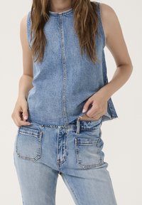 Denim ärmlös topp i ljusblå med en framsöm och rå kant. Matchas med ljusblå jeans som har bakfickor och fransdetaljer.