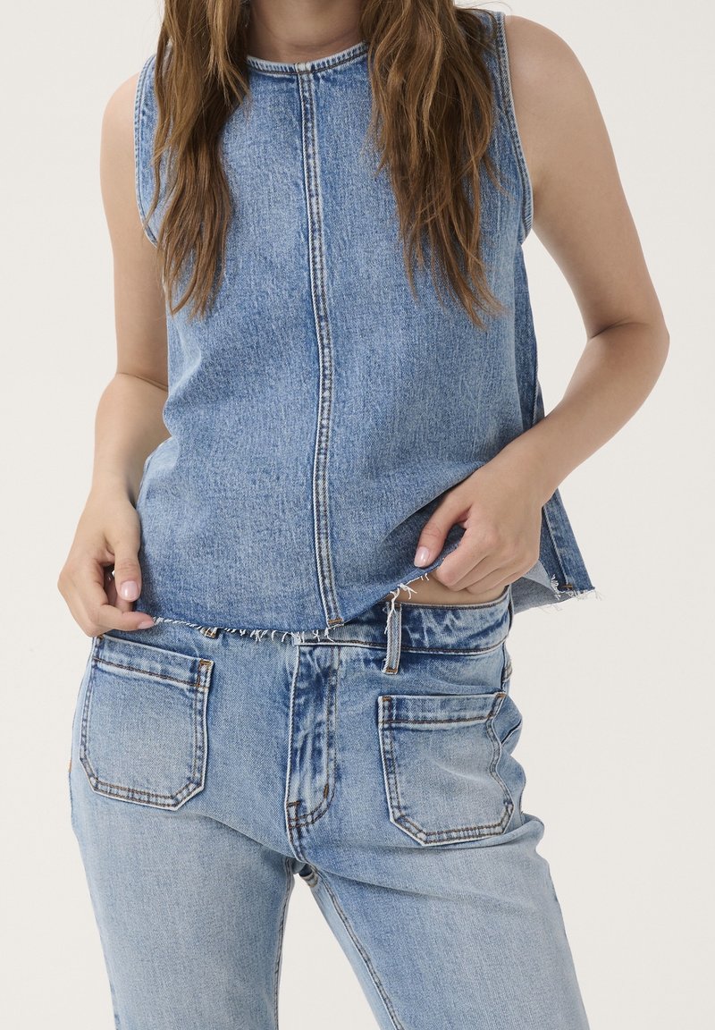 Denim ärmlös topp i ljusblå med en framsöm och rå kant. Matchas med ljusblå jeans som har bakfickor och fransdetaljer.