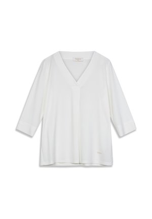 Blouse blanche à col en V avec manches trois-quarts, texture lisse, coupe ample, avec une petite étiquette de marque sur le bord inférieur.