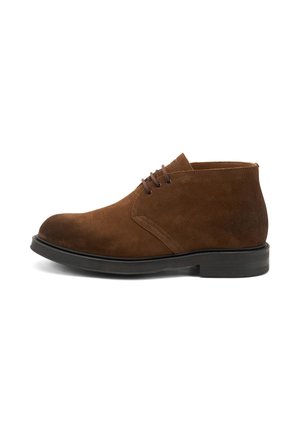 Botas de ante marrón hasta el tobillo con punta redonda, cordones en la parte delantera y una suela de goma negra, presentadas sobre un fondo blanco.