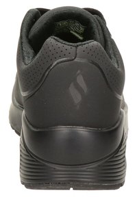 Zapato deportivo negro con parte superior sintética suave, detalles perforados, collar acolchado y suela de goma texturizada. Diseño minimalista.