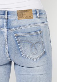 Light blue denim jeans with a decorative back pocket stitch detail and a brown leather brand label at the waistband.