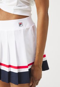 Gonna bianca a pieghe con strisce orizzontali rosse e blu navy, dotata di una cintura piatta e di un'etichetta con logo. Realizzata in materiale liscio e leggero.