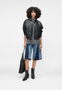 Mustast kunstnahast lühikeste varrukatega jakk nööpide ees, hall t-särk, mustrilised sinised teksapüksid, ning mustad kõrge säärega saapad. Must kott.