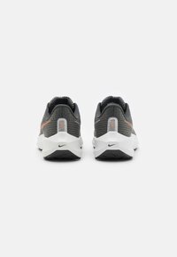 Zapatillas deportivas grises con parte superior texturizada, acento naranja, mediasuela blanca y suela de goma negra, vistas desde atrás. Logotipo de Nike visible.