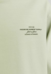 Felpa verde chiaro con una texture morbida. Presenta un logo stampato di colore verde scuro che recita "Fornitura di Abbigliamento Premium, Jack & Jones."
