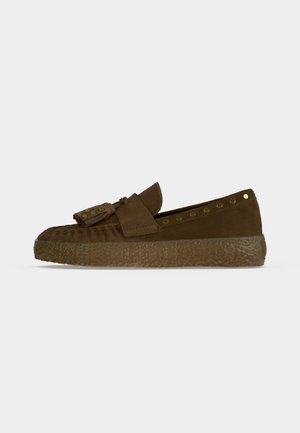 Mocassin en daim marron avec pompon et clous dorés, semelle épaisse texturée et détails cousus sur un fond uni.