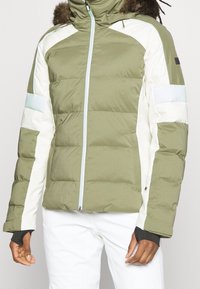 Giacca imbottita con corpo verde, maniche bianche e dettagli azzurri. Presenta un design imbottito, chiusura con zip e cappuccio regolabile con pelliccia sintetica.