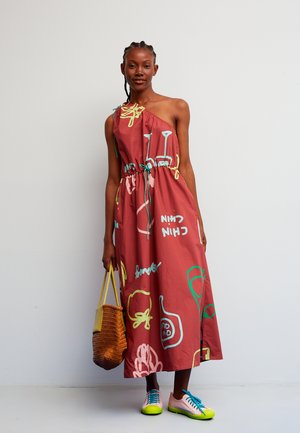 Vestido burdeos de un solo hombro con patrones abstractos coloridos, ajustado en la cintura. Combina con zapatos rosa y verde neón y un bolso tejido.