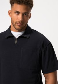 Polo shirt nero a maniche corte con collo a zip quarti, dotato di taschino sul petto e realizzato in un tessuto morbido e testurizzato, con una vestibilità comoda.